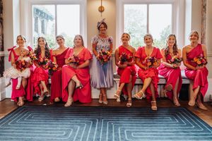 Wedding party members in matching red dresses sit together on a wooden porch for a group photo.