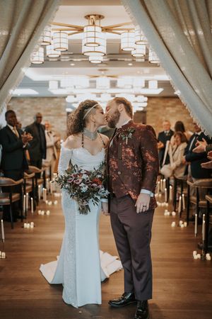 A romantic first dance moment between newlyweds on a wooden dance floor with guests watching in the background.