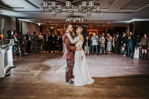 A couple shares their first dance on a dimly lit dance floor while wedding guests watch from the sidelines.