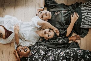 Group of friends lying on wooden floor in casual attire while relaxing together and smiling at camera.