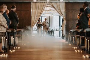 Elegant wedding reception venue with exposed brick walls and long tables set for dining with glowing candles and white decor.