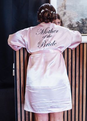 Pink satin bridal party robes with elegant embroidered text displayed on wooden hangers in a row.