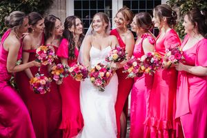 Wedding party wearing vibrant pink dresses holding beautiful pink and red floral bouquets at an outdoor venue.