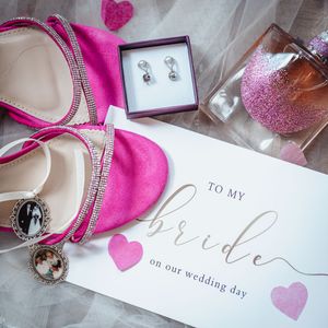 Pink and white wedding accessories including glittery shoes, jewelry, and cards arranged on a light background.