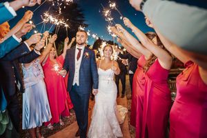 Wedding guests hold sparklers creating a magical tunnel of light during an evening celebration.