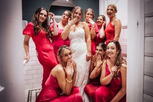 A group of bridesmaids in red dresses pose playfully with the bride in white at a wedding celebration.