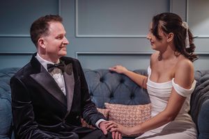 A couple shares an intimate moment while sitting together on a gray tufted couch during their wedding celebration.