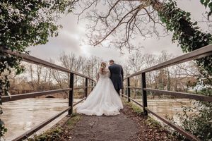 Wedding couple walking along rustic wooden bridge surrounded by trees and natural scenery.