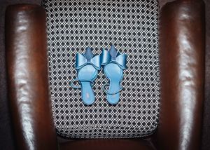 Light blue flip flops resting on a gray patterned cushion between brown leather armrests.