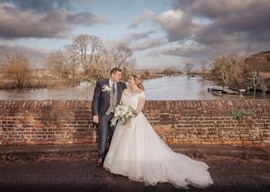 A romantic wedding couple poses against a rustic brick wall during their outdoor winter photo session.
