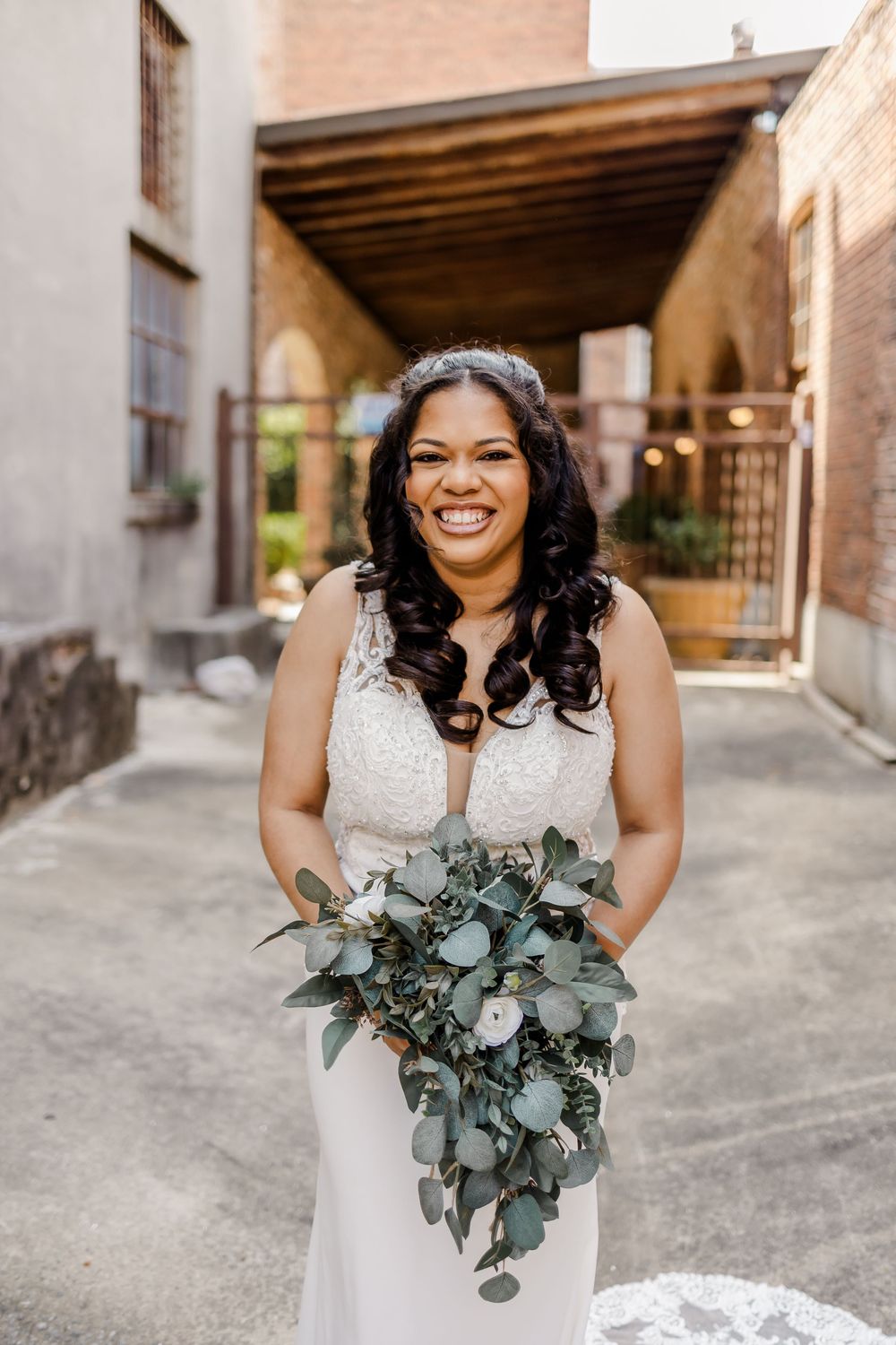 Bride holding eucalyptus bouquet poses in front of rustic brick archways.