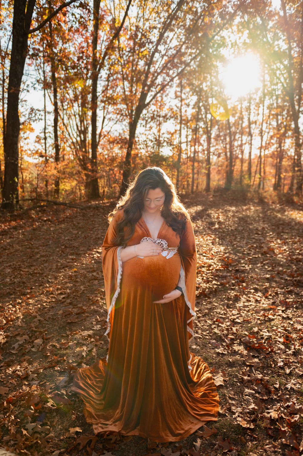 An elegant portrait session in a forest with autumn leaves and golden sunlight.