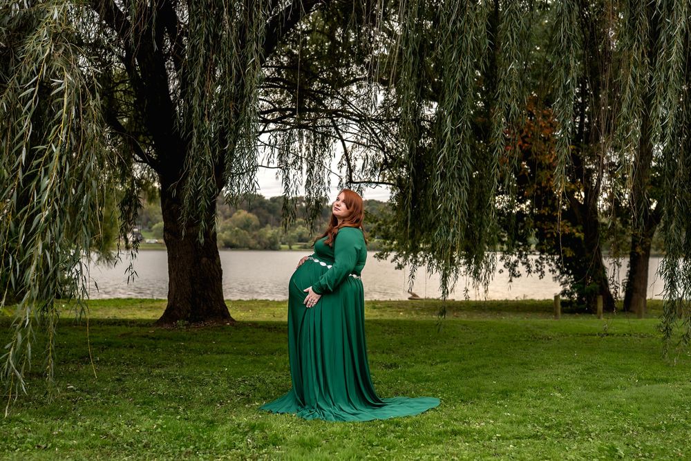 A couple in emerald green attire poses beneath a weeping willow tree for romantic outdoor photos.