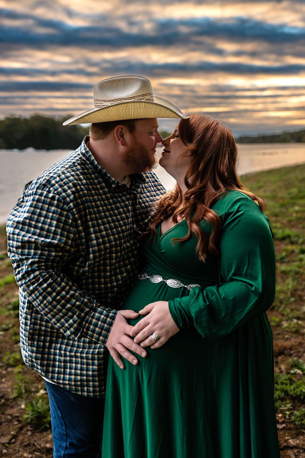 A couple in a green sweater and plaid shirt share romantic moments at sunset by a lake in a series of photos.
