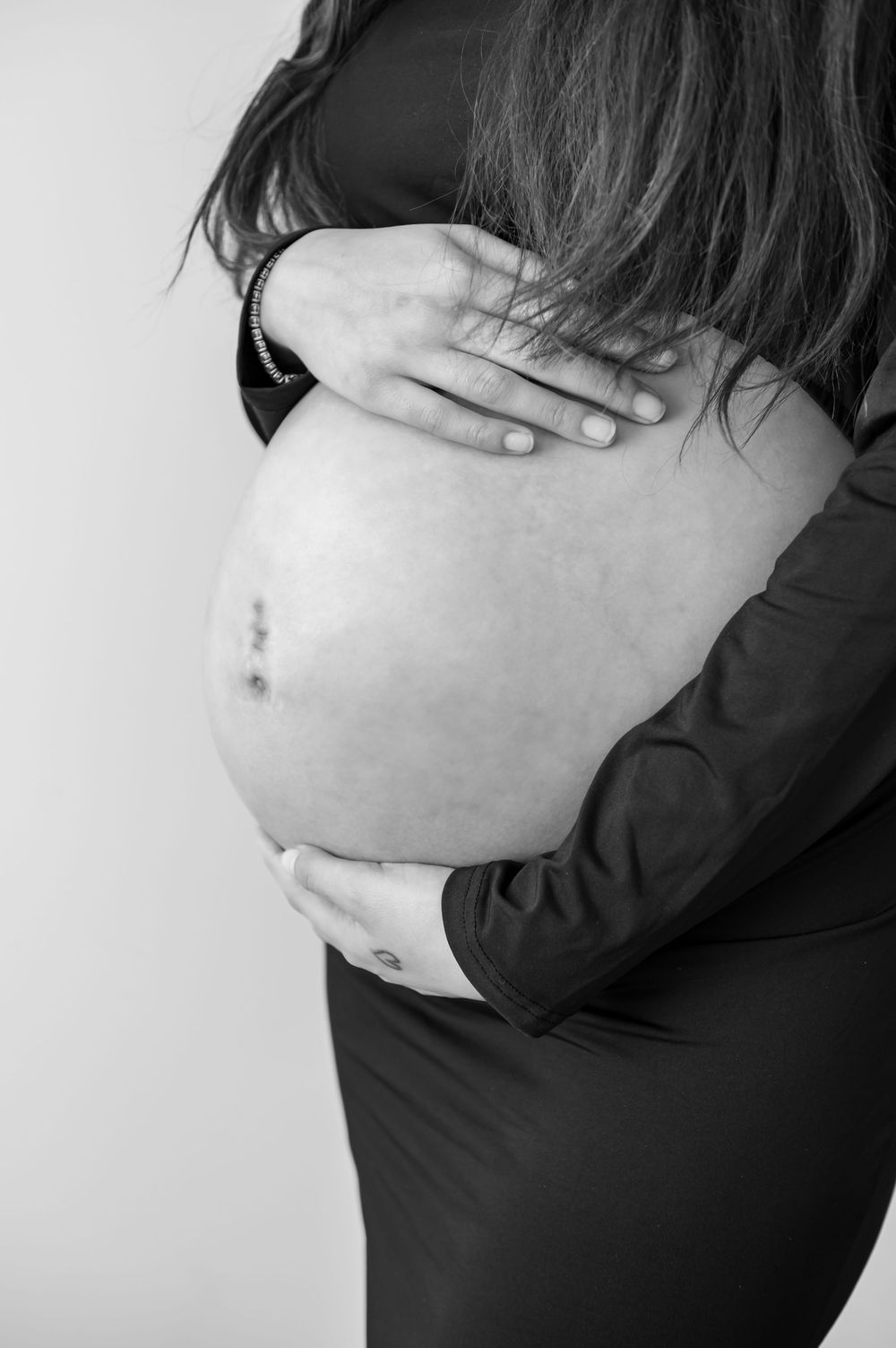 Close-up black and white photography highlighting a pregnant belly against a light background.