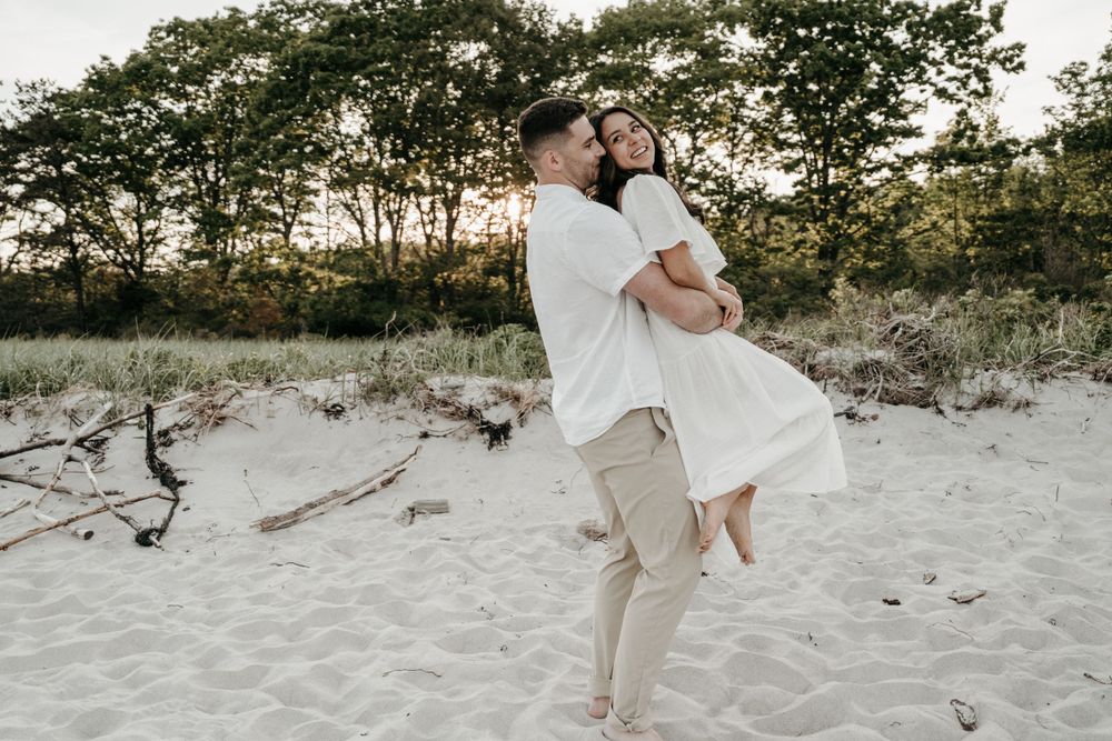 Couple embracing on sandy beach with trees silhouetted in background during golden hour.