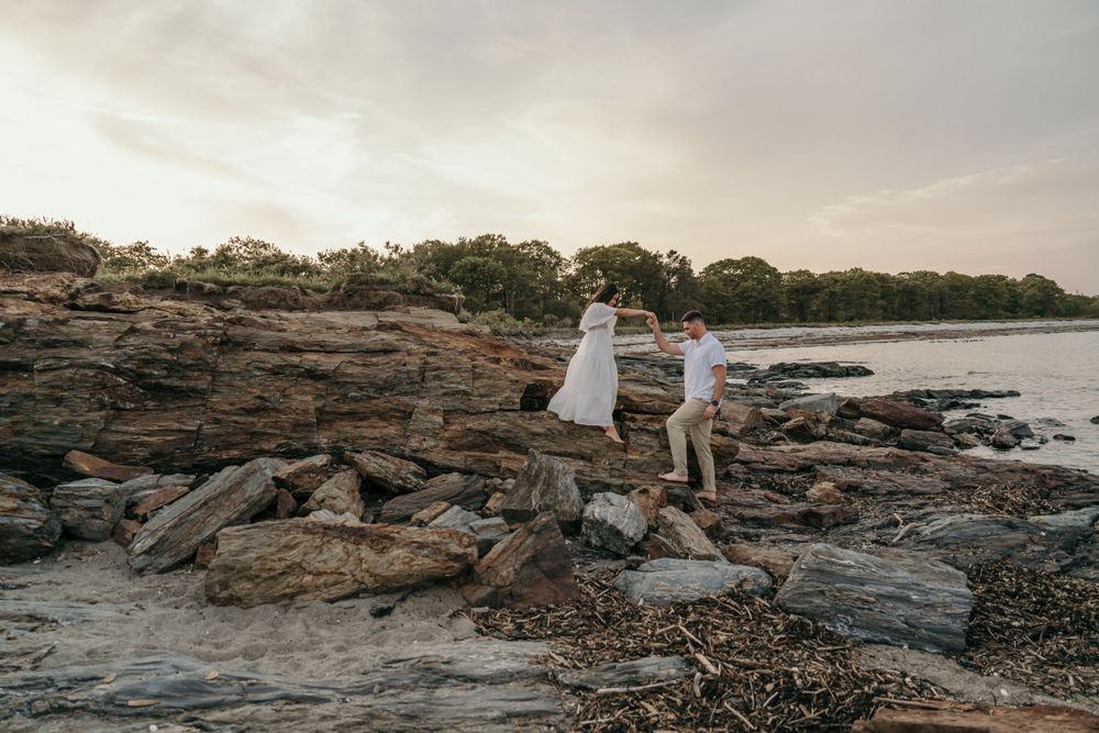 A couple stands on rocky coastal terrain at sunset.