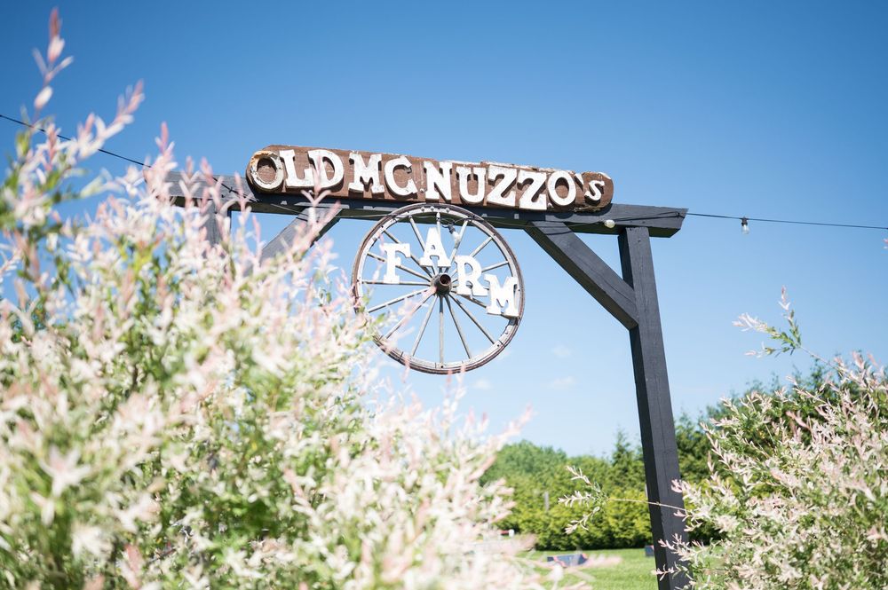 Rustic wooden sign reading 'Old Nuzzo's' against a bright blue sky with blossoming trees. Nuzzo's Farm Branford Connecticut