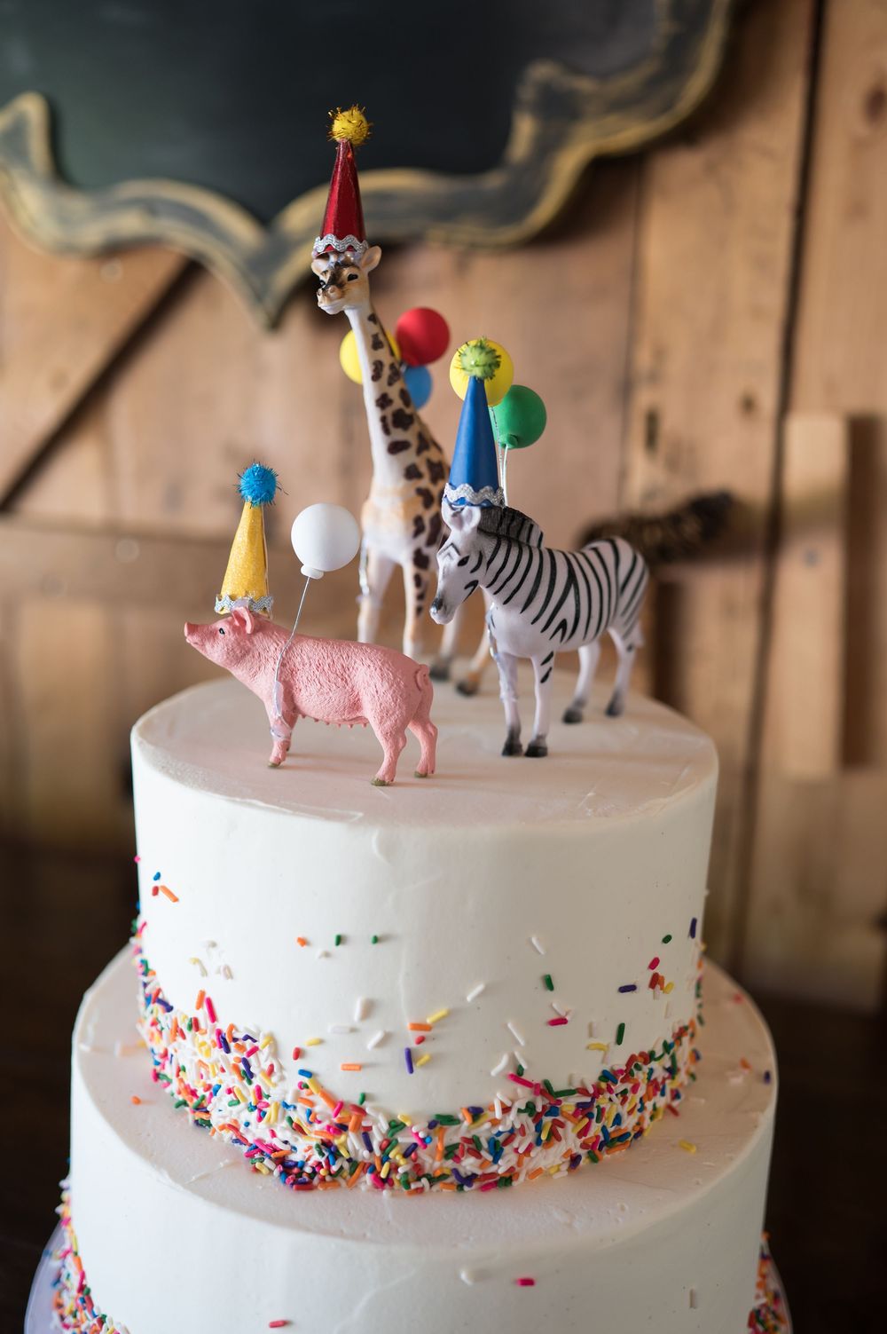 White birthday cake decorated with colorful sprinkles and animal figurine toppers including a zebra and pig. Nuzzo's Farm Branford Connectic