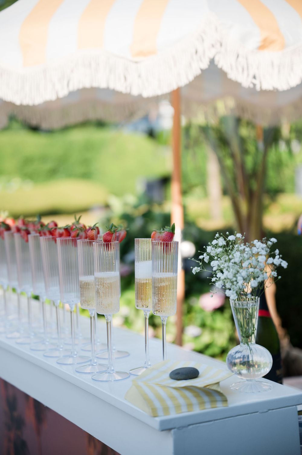 Elegant outdoor party setup with glass champagne flutes and white floral arrangements.