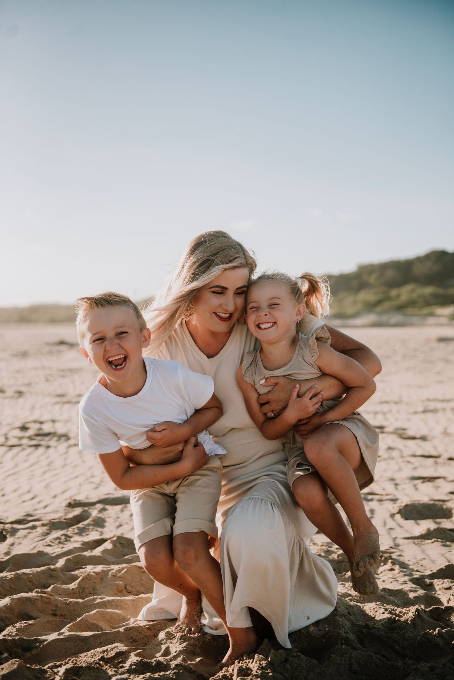 A mother on the beach holding her son and daughter as they laugh hysterically with joy on Hartenbos beach