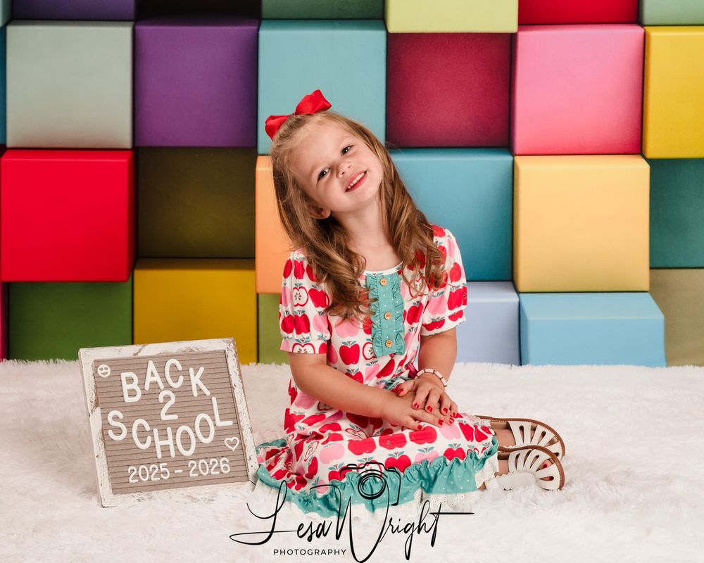A joyful student poses against a colorful block wall with a 'Back to School' sign for first day photos.