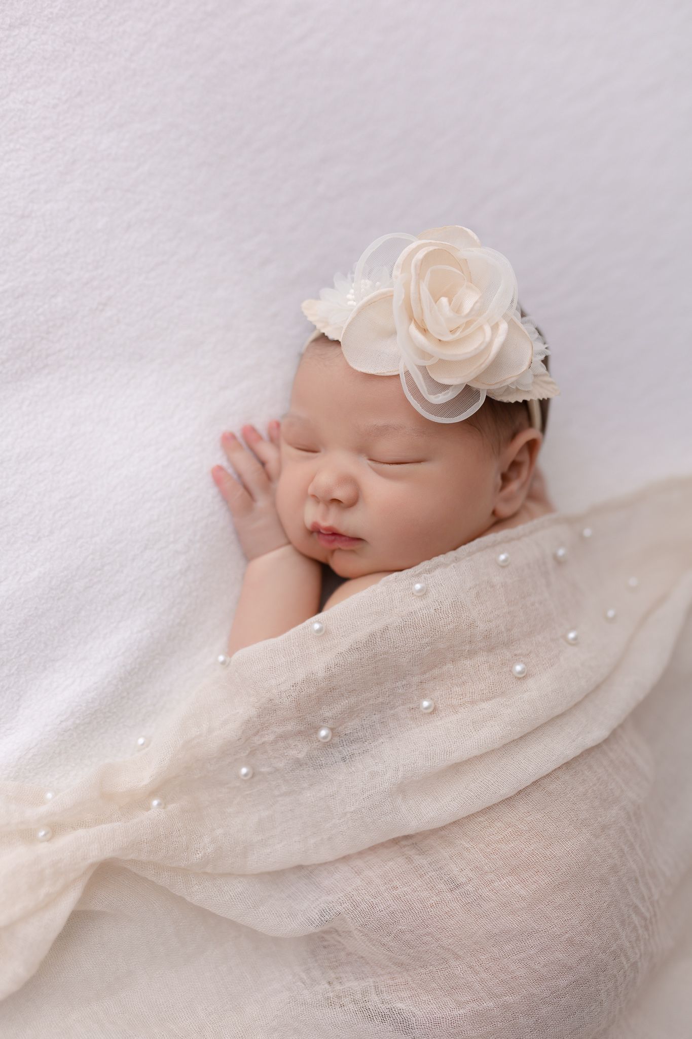 Parents in white attire lovingly holding their newborn baby against a neutral beige backdrop.