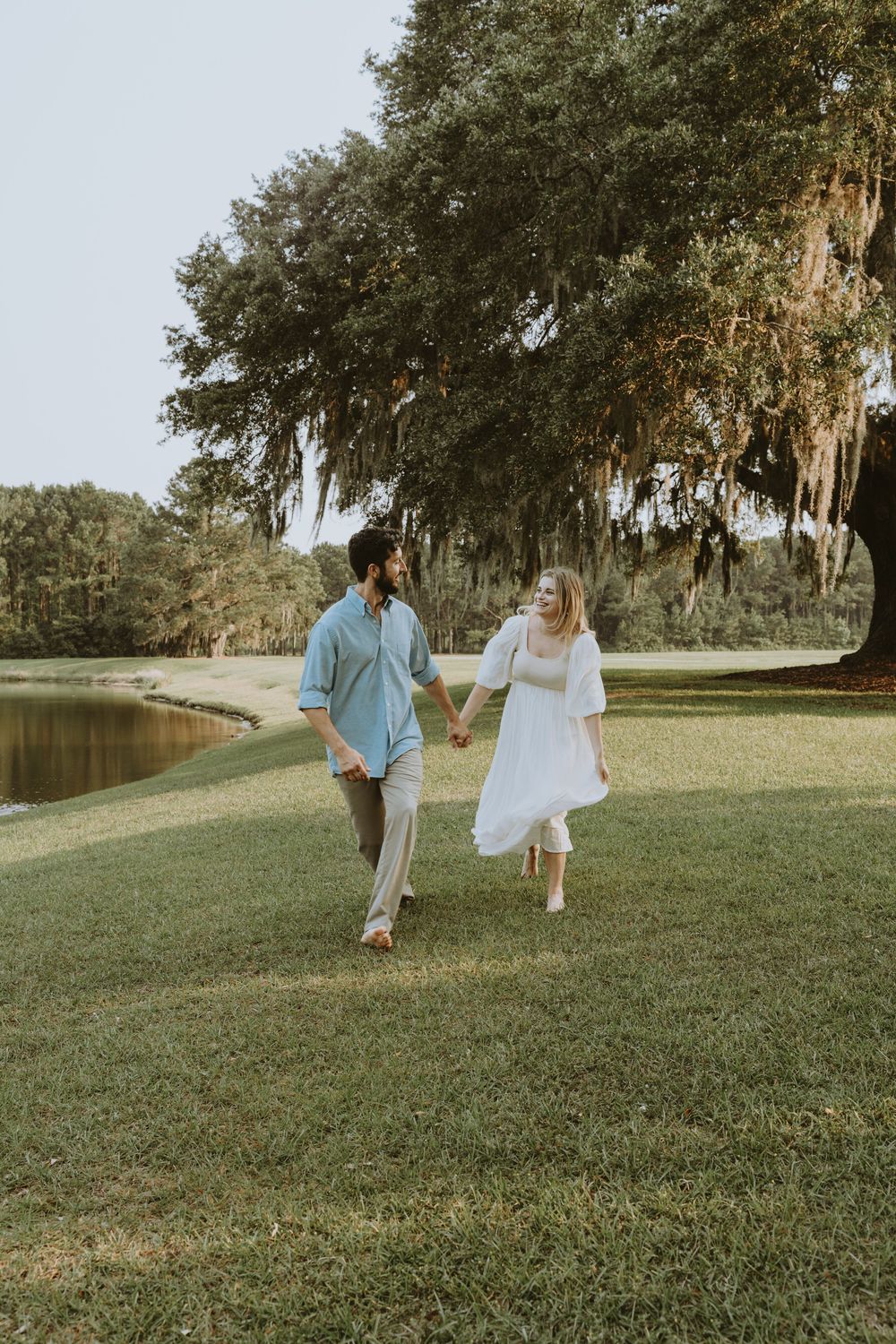 A couple walking together on a grassy hill with moss-covered trees in the background.