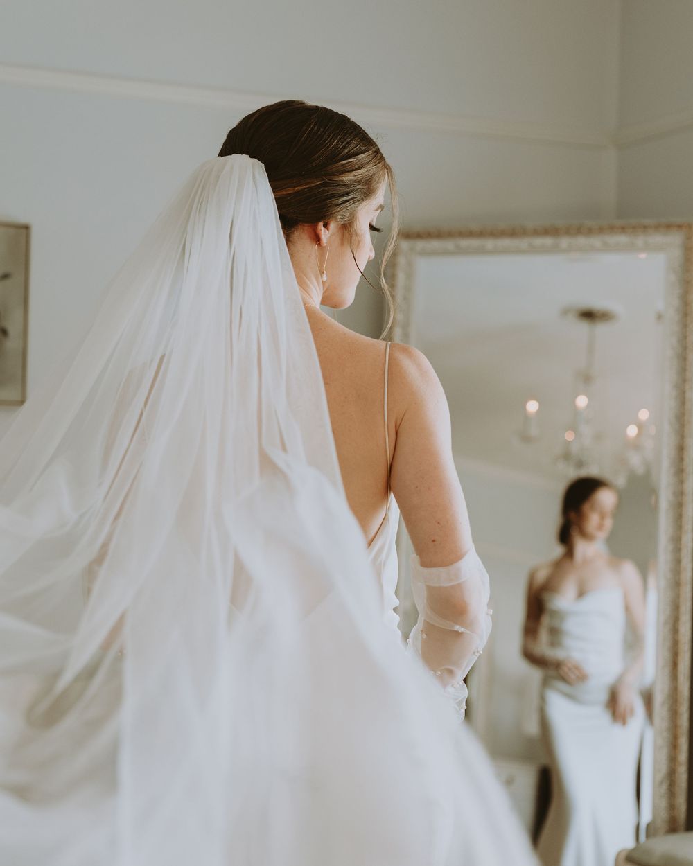 A flowing white wedding dress and veil captured in an elegant indoor setting.