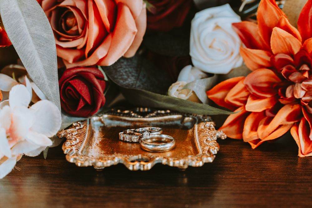 Wedding rings and orange flowers arranged on dark surface for detail photography.