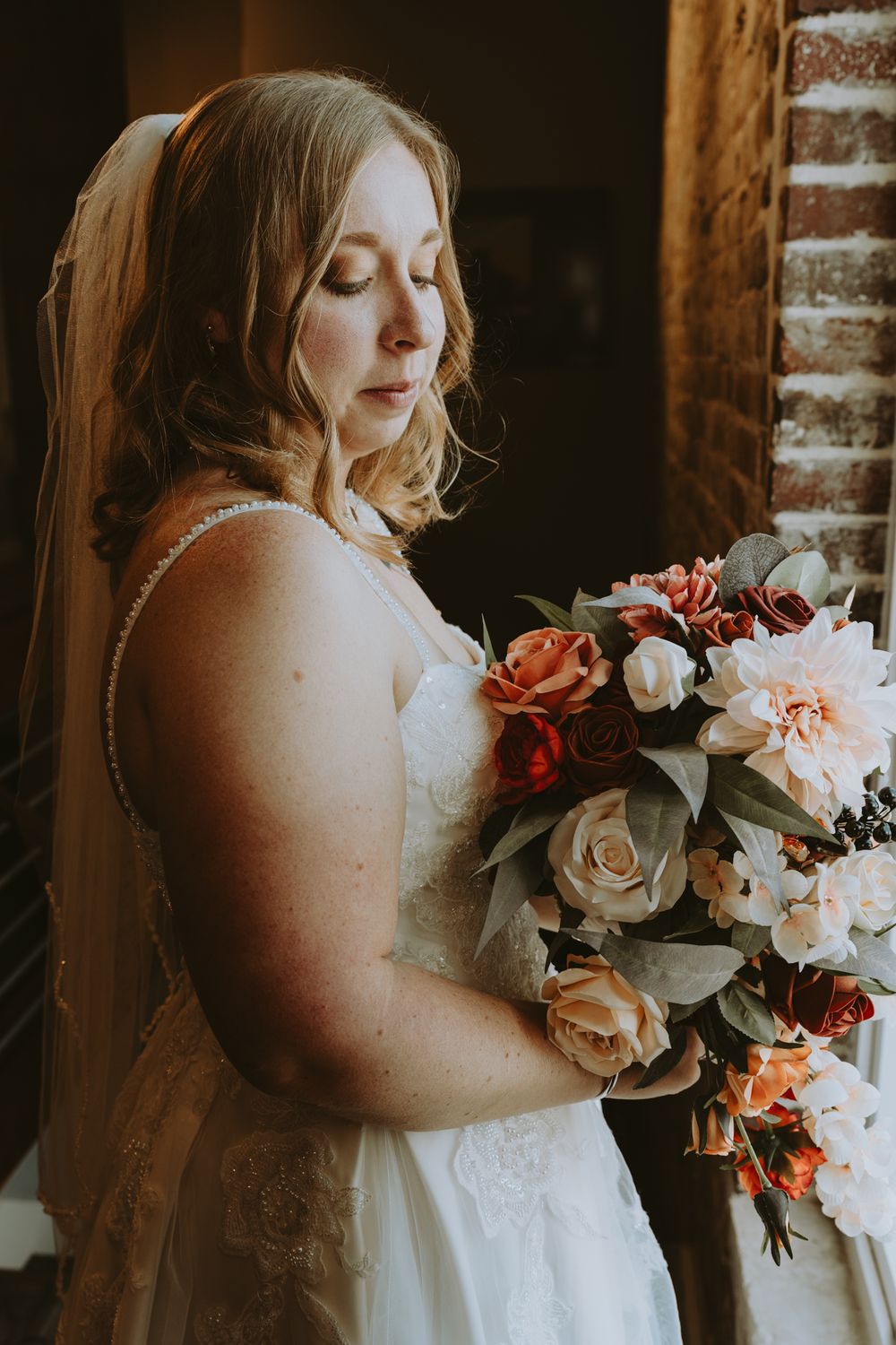 Close-up shots of bridal bouquet with coral and white roses against rustic brick wall.