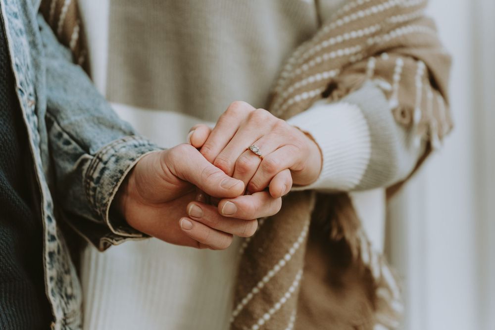 Close-up of hands displaying engagement ring with soft sweater and denim jacket details.