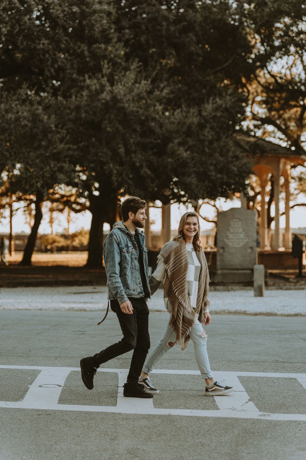 Couple walking together on concrete path surrounded by trees at sunset.