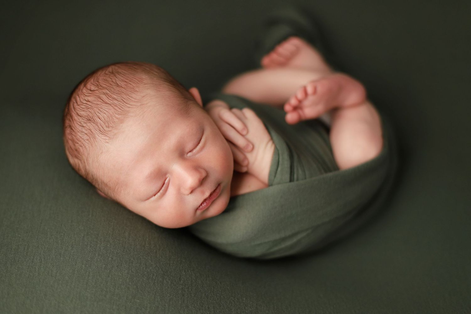 Newborn baby rests peacefully on sage green fabric in artistic side-profile poses during professional photo session.