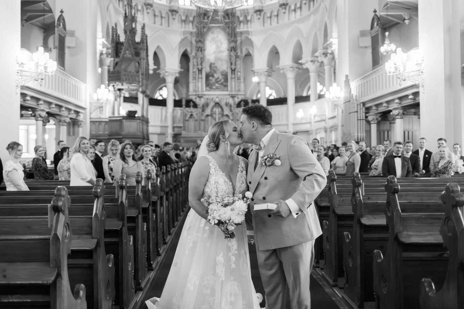 A wedding ceremony captured in black and white inside a grand church with ornate architecture.
