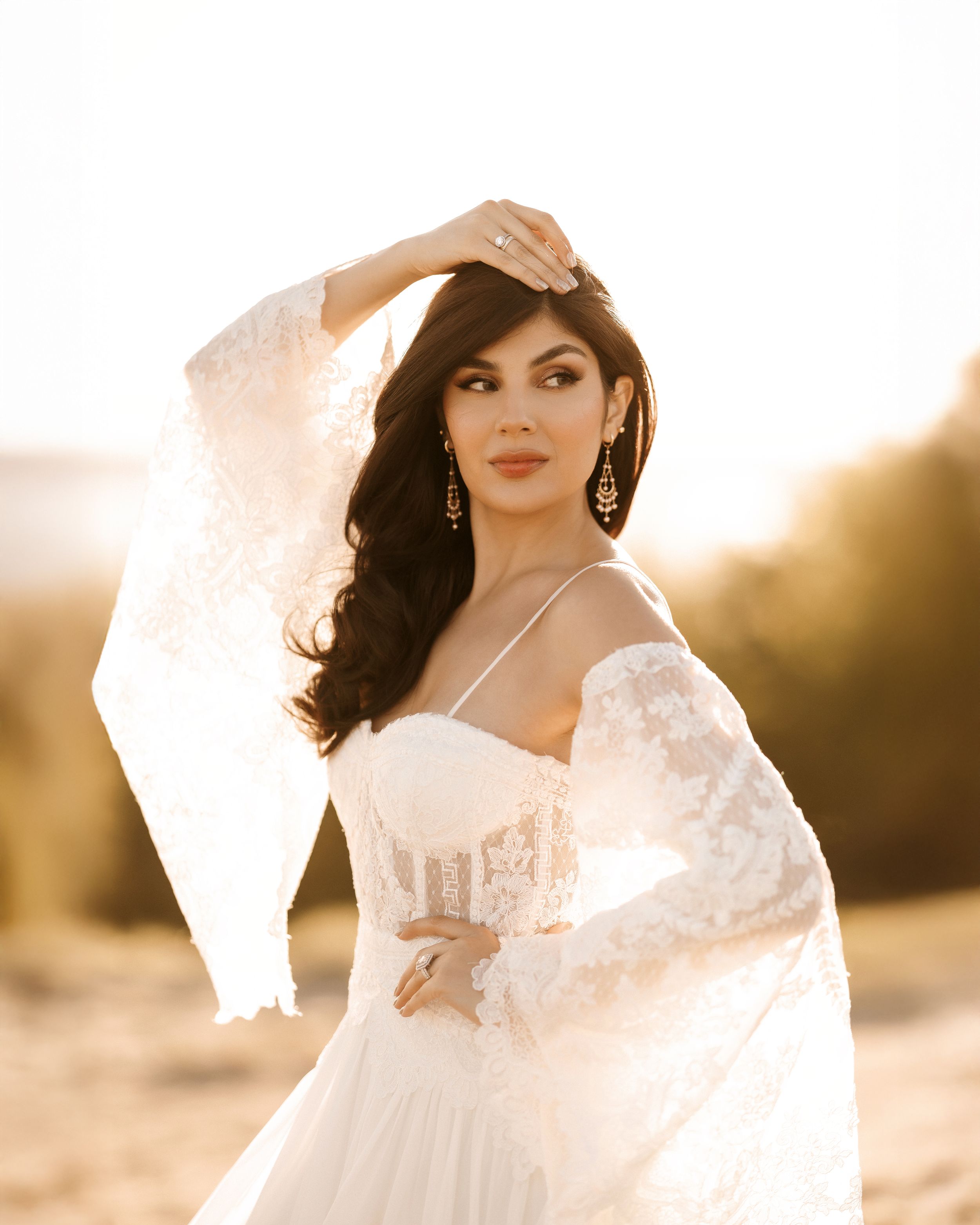 A person in a flowing white lace dress poses elegantly against a golden sunset backdrop.