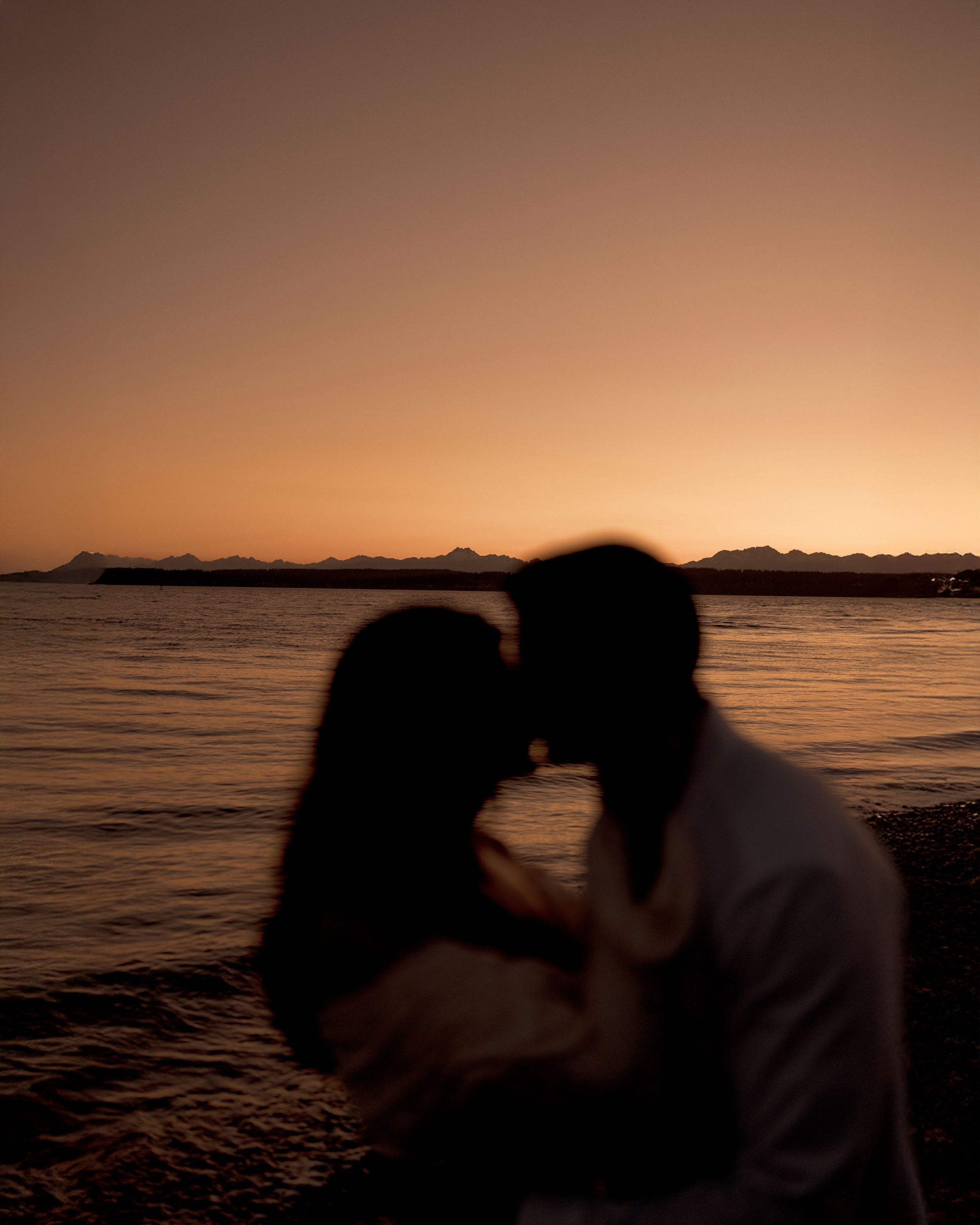 Silhouette of a couple sharing an intimate moment at sunset by the water's edge.