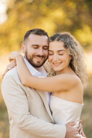 A loving couple embraces and smiles with their eyes closed in warm golden sunlight, sharing a romantic moment together.