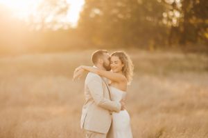 A romantic sunset photo of a couple embracing in a golden field during their wedding photoshoot.