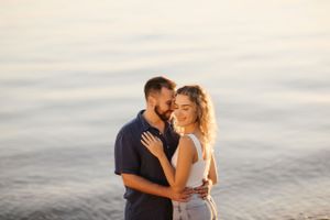 Romantic couple embraces on beach at sunset with ocean waves in background.