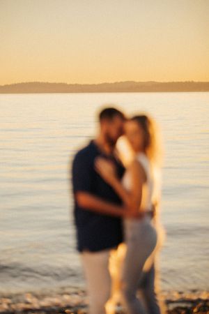Blurred silhouette of a romantic couple embracing at sunset by a calm waterfront on a golden evening.