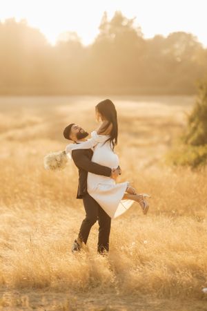 A couple embraces in a golden field at sunset with backlit glowing light creating a romantic silhouette.