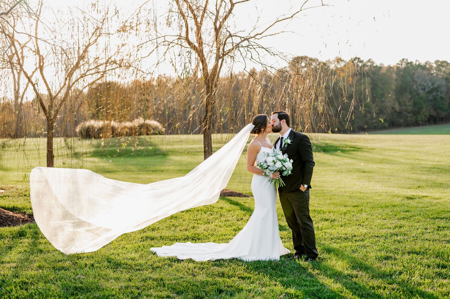 Long flowing wedding veil trailing dramatically across a green field at sunset.