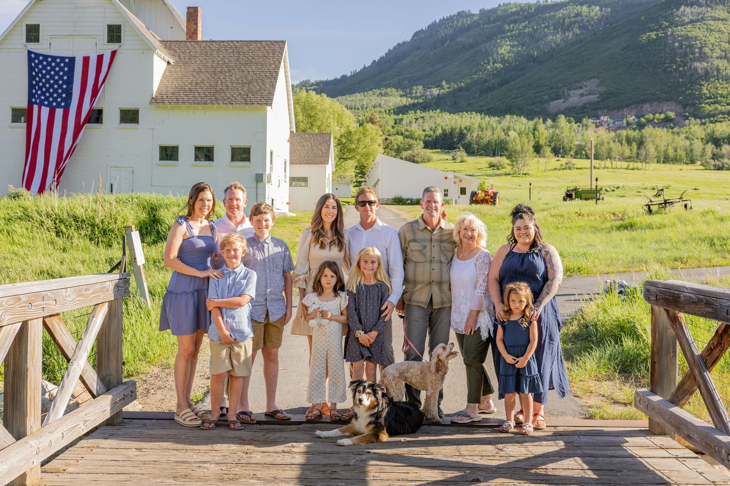 Group photo of people gathered outside a white barn with American flags and mountain backdrop.