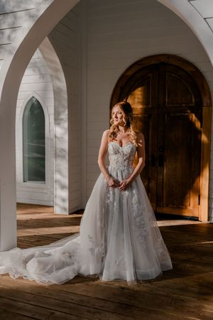 A bride in a flowing tulle gown poses gracefully under arched stone corridors with dramatic lighting and shadows.