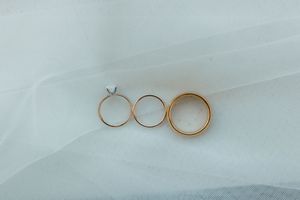 Three gold wedding and engagement rings arranged on white bridal veil fabric, including a diamond solitaire ring.