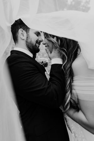 Black and white wedding photograph showing an intimate moment between newlyweds under a flowing veil.
