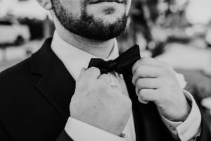 A group of groomsmen in black tuxedos and bow ties pose together while adjusting their ties in a formal setting.
