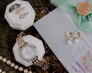 Elegant wedding details including pearl jewelry, delicate stationery, and mint green accents arranged on a dark surface.