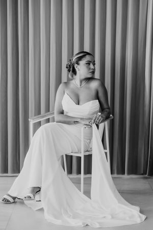 Elegant bride in a strapless white gown sits gracefully on a chair in a black and white portrait photo.